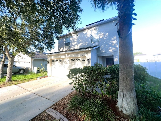 traditional-style home with a garage, driveway, fence, and stucco siding