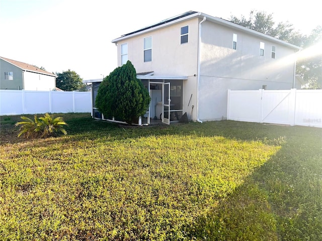 rear view of property featuring a sunroom, a fenced backyard, a lawn, and stucco siding