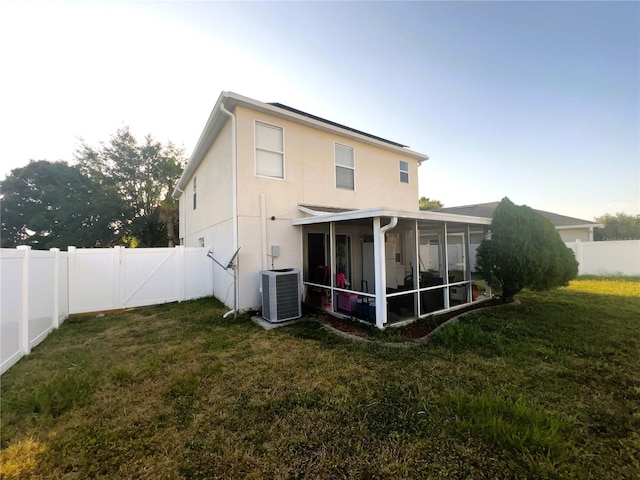 rear view of property featuring a sunroom, a fenced backyard, a lawn, and central air condition unit