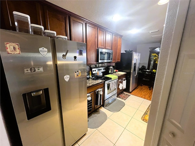 kitchen with appliances with stainless steel finishes, stone counters, and light tile patterned flooring