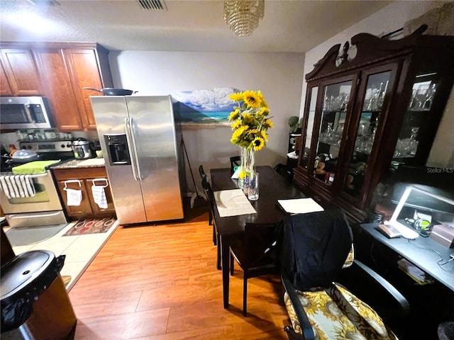 kitchen featuring brown cabinets, light countertops, light wood-style flooring, appliances with stainless steel finishes, and glass insert cabinets