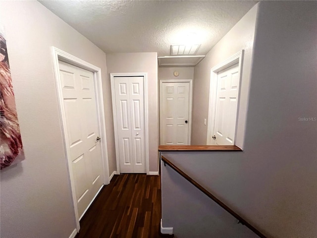 corridor with visible vents, dark wood finished floors, a textured ceiling, and baseboards