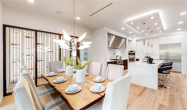 dining room featuring a chandelier, light wood-type flooring, a tray ceiling, and sink