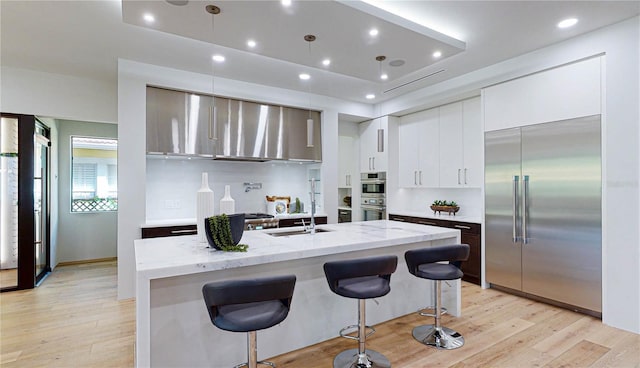 kitchen featuring light stone countertops, stainless steel appliances, a raised ceiling, white cabinets, and an island with sink