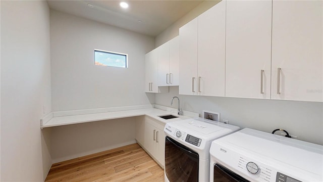 clothes washing area with washer and clothes dryer, light hardwood / wood-style flooring, cabinets, and sink