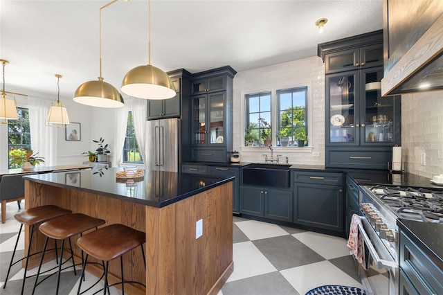 kitchen featuring wall chimney exhaust hood, premium appliances, sink, decorative light fixtures, and a center island