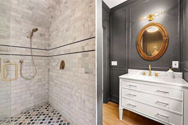 bathroom with a tile shower, vanity, and wood-type flooring