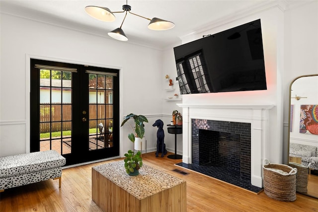 living room with light hardwood / wood-style floors, crown molding, a tile fireplace, and french doors