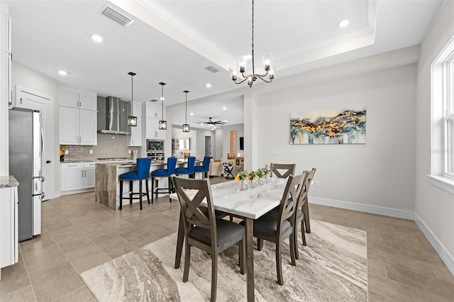 tiled dining room with ceiling fan with notable chandelier, crown molding, and a tray ceiling