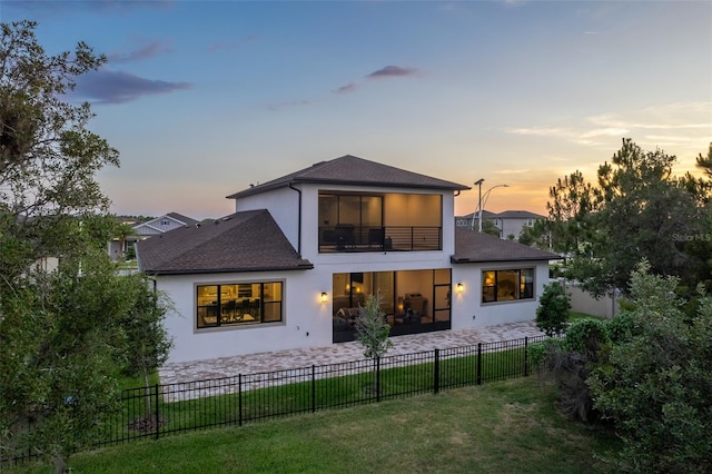 back house at dusk with a balcony, a yard, and a patio