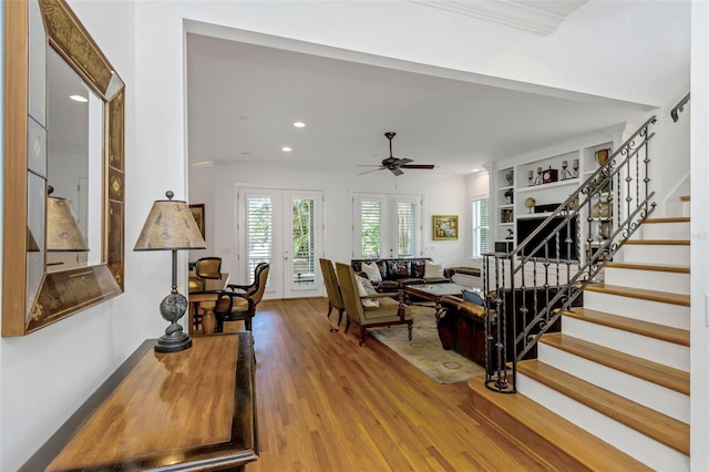 living room with built in shelves, ceiling fan, french doors, crown molding, and hardwood / wood-style floors