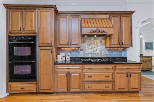 kitchen with decorative backsplash, custom exhaust hood, crown molding, black appliances, and dark stone countertops