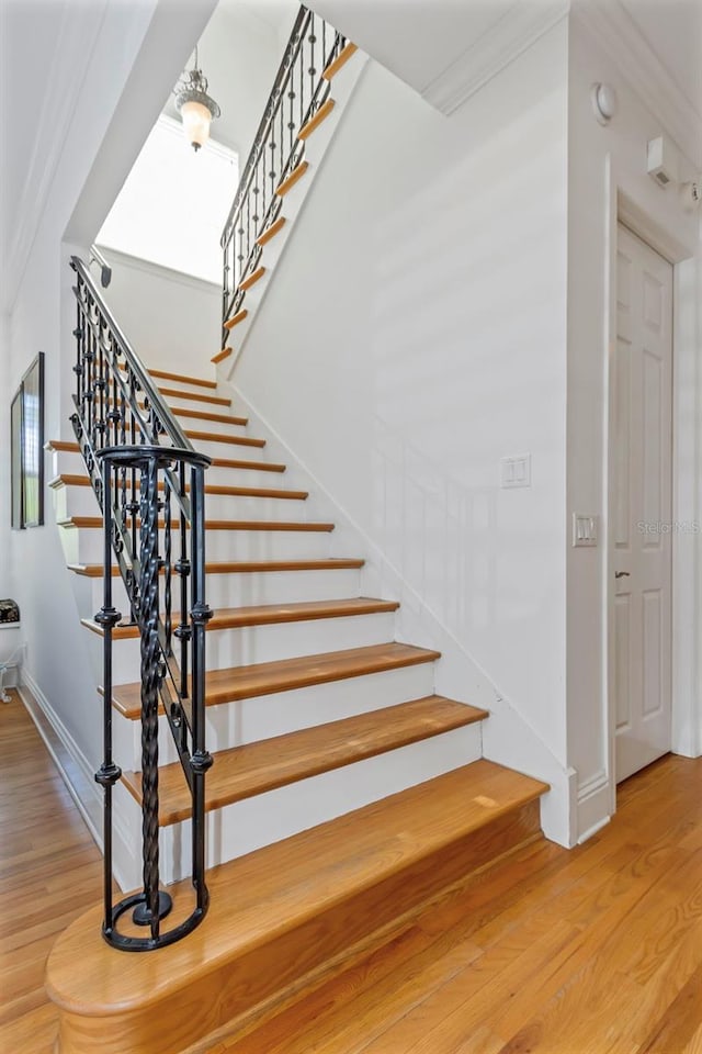 stairway with crown molding and wood-type flooring