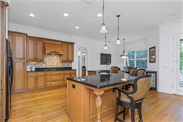 kitchen featuring decorative light fixtures, premium range hood, an island with sink, and ornamental molding