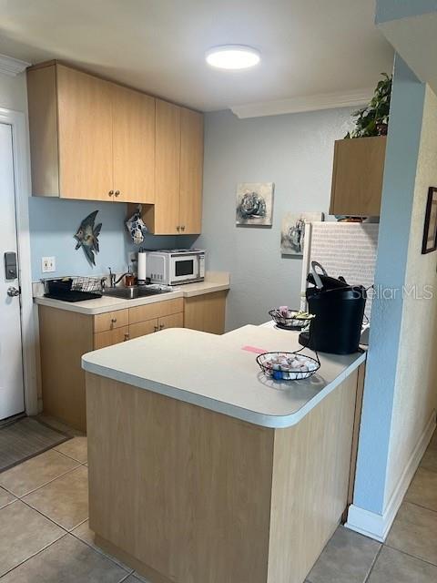 kitchen with kitchen peninsula, ornamental molding, sink, and light tile patterned floors