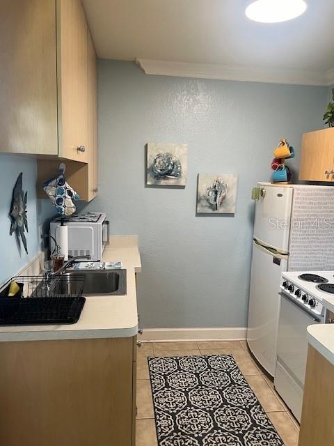 kitchen with white range, crown molding, light tile patterned flooring, and sink