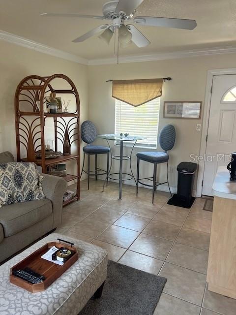 tiled living room with ceiling fan and ornamental molding