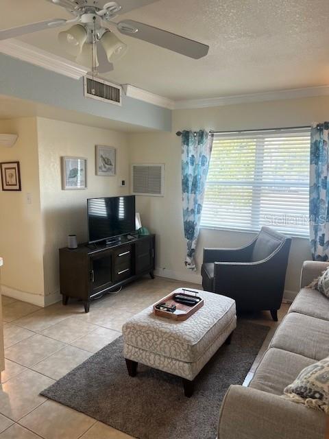 living room with ornamental molding, ceiling fan, light tile patterned floors, and a textured ceiling