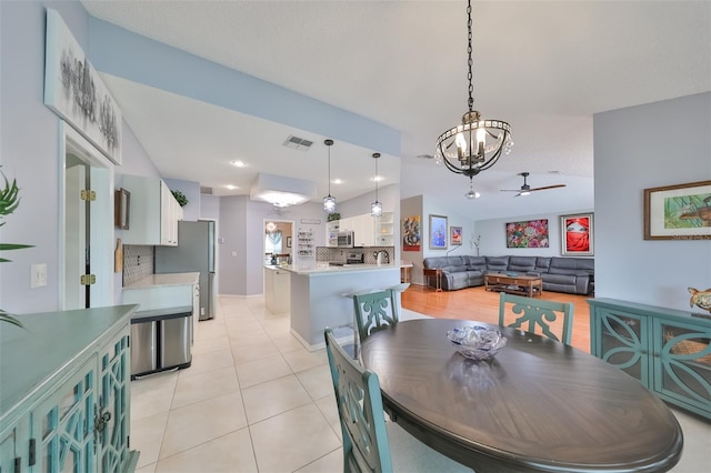 tiled dining space with ceiling fan with notable chandelier and lofted ceiling