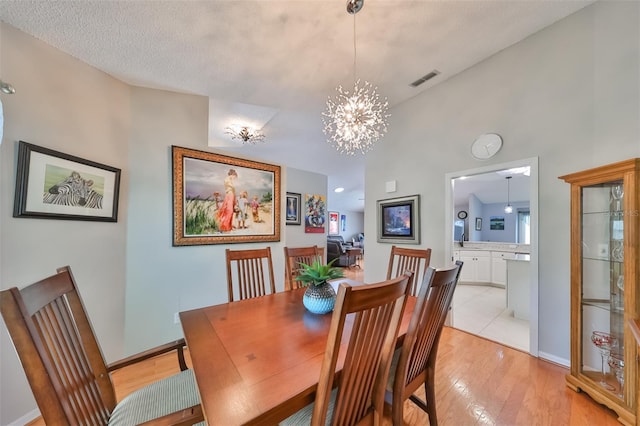 dining space featuring a notable chandelier, vaulted ceiling, a textured ceiling, and light hardwood / wood-style flooring