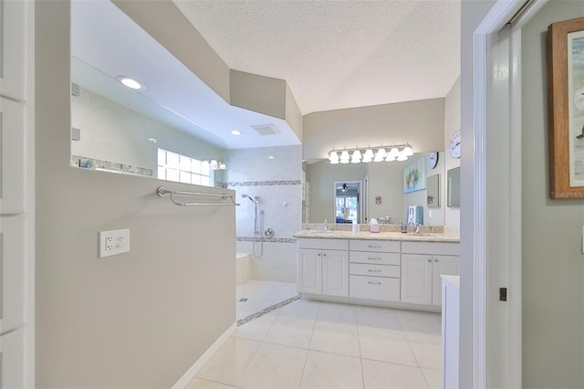 bathroom with tile patterned flooring, a tile shower, a textured ceiling, and vanity