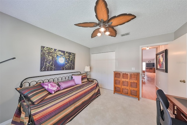 bedroom featuring ceiling fan, a closet, light carpet, and a textured ceiling