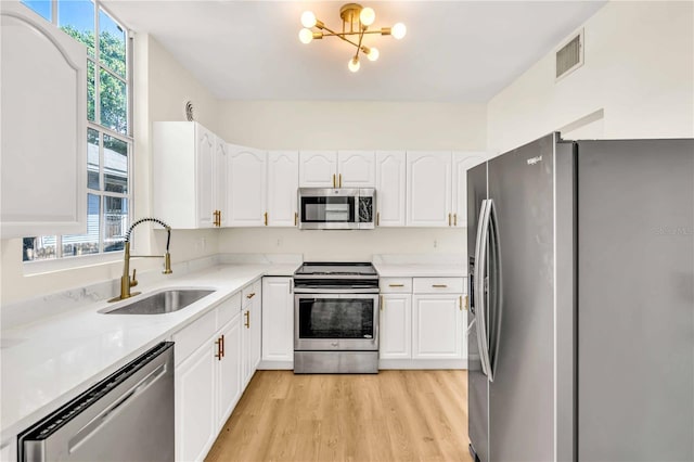 kitchen featuring sink, appliances with stainless steel finishes, white cabinetry, a notable chandelier, and light wood-type flooring