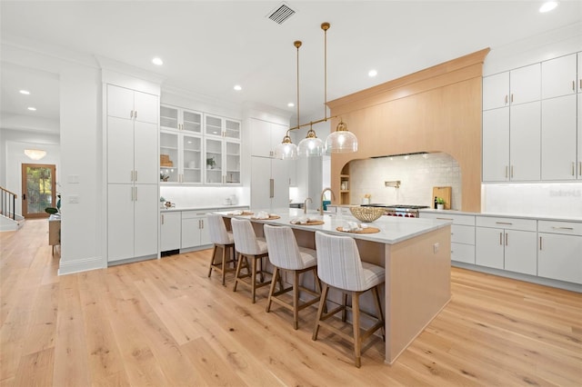 kitchen featuring a kitchen island with sink, light hardwood / wood-style floors, white cabinets, a kitchen bar, and decorative light fixtures