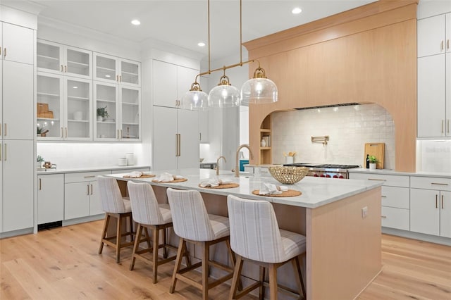 kitchen featuring decorative light fixtures, an island with sink, a breakfast bar area, white cabinets, and paneled built in refrigerator