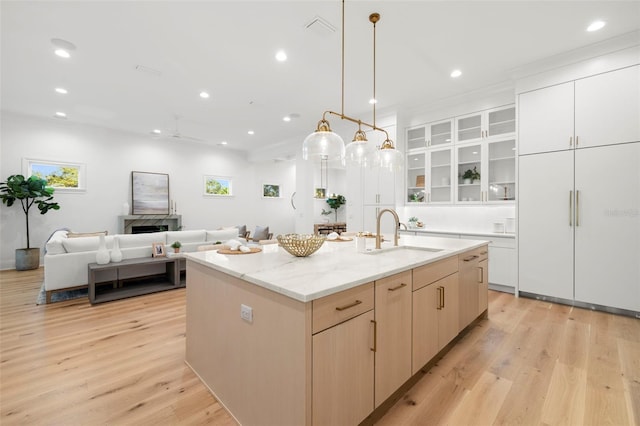 kitchen featuring sink, hanging light fixtures, a wealth of natural light, light hardwood / wood-style floors, and a center island with sink