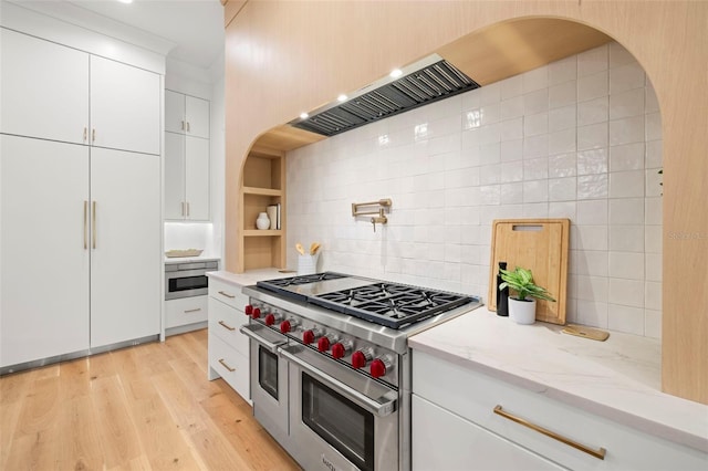 kitchen featuring white cabinetry, range with two ovens, light stone counters, tasteful backsplash, and light wood-type flooring