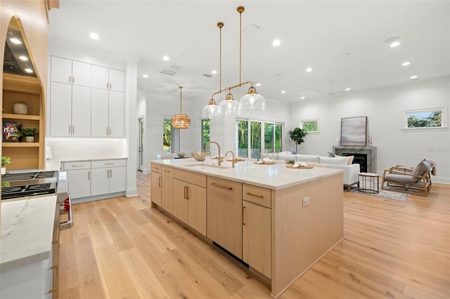 kitchen featuring sink, hanging light fixtures, a center island with sink, light hardwood / wood-style flooring, and light stone countertops