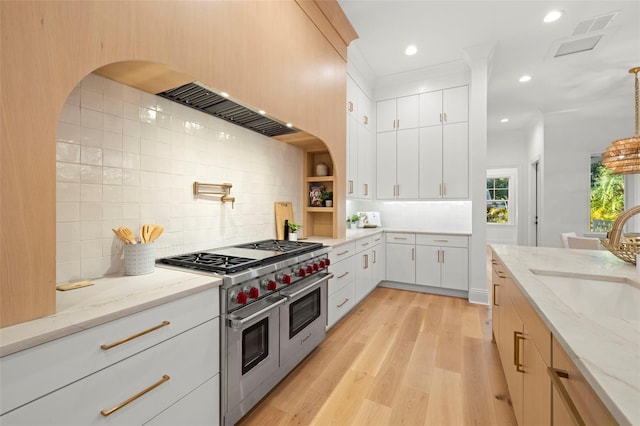 kitchen with sink, white cabinetry, hanging light fixtures, light stone counters, and range with two ovens