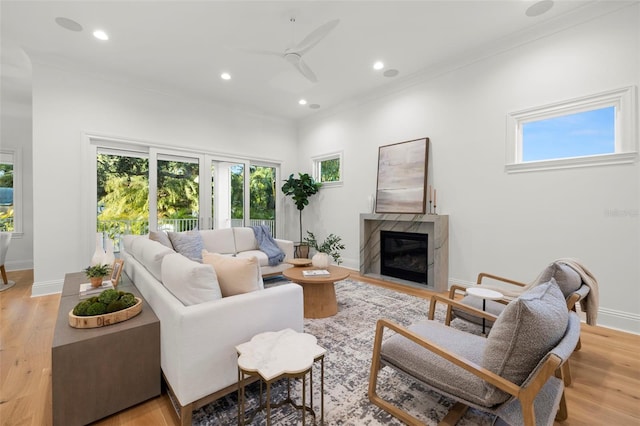 living room featuring a premium fireplace, ornamental molding, ceiling fan, and light hardwood / wood-style flooring