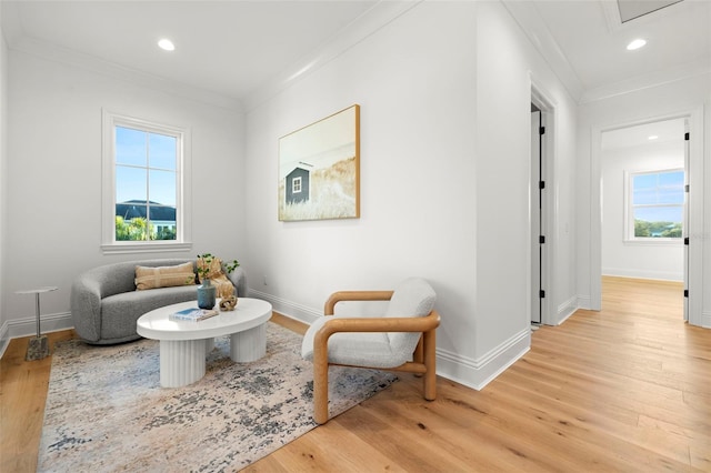 living area with crown molding, plenty of natural light, and light hardwood / wood-style floors