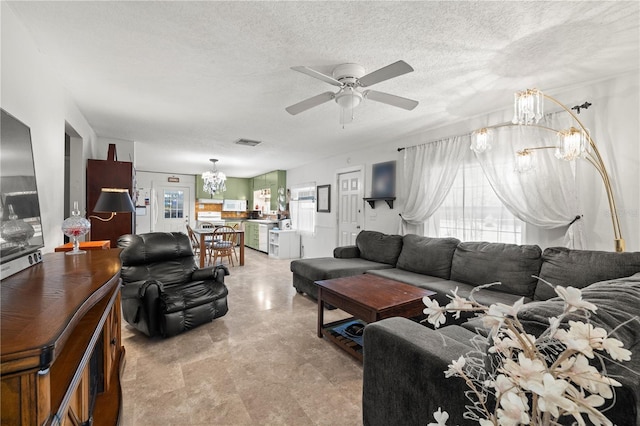 living room with ceiling fan with notable chandelier and a textured ceiling