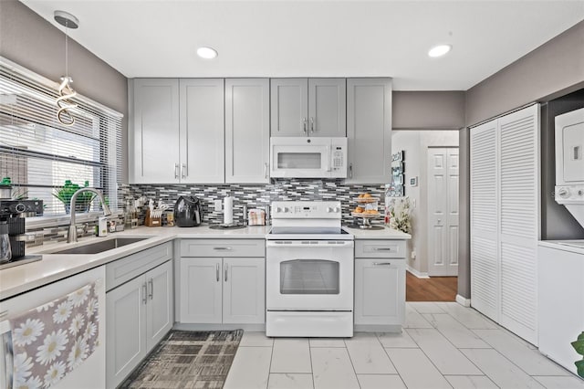 kitchen with white appliances, sink, stacked washer and dryer, hanging light fixtures, and gray cabinets