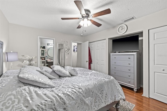 bedroom with ensuite bathroom, a textured ceiling, two closets, ceiling fan, and wood-type flooring