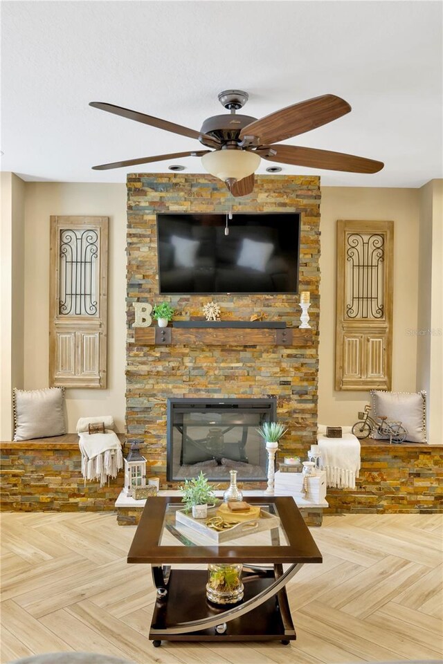 living room with ceiling fan, parquet flooring, and a stone fireplace