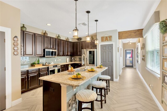 kitchen featuring appliances with stainless steel finishes, a kitchen bar, a center island with sink, and light parquet flooring