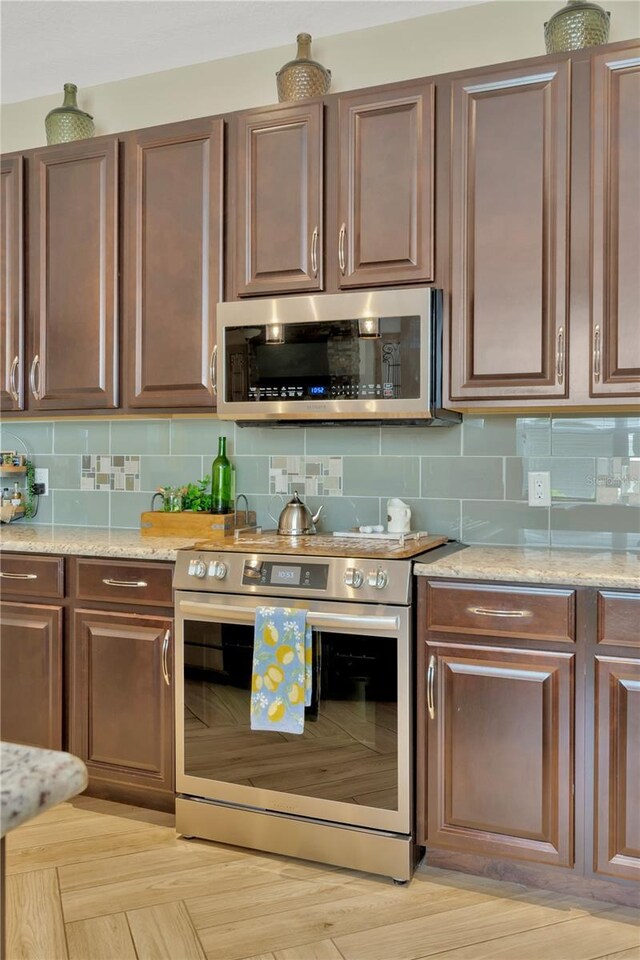 kitchen featuring backsplash, light stone counters, stainless steel appliances, and light hardwood / wood-style floors