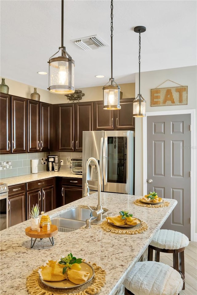 kitchen with light hardwood / wood-style floors, stainless steel refrigerator, sink, pendant lighting, and a breakfast bar