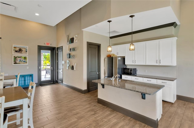 kitchen featuring an island with sink, stainless steel refrigerator, dark stone counters, and light hardwood / wood-style floors