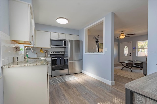 kitchen with appliances with stainless steel finishes, tasteful backsplash, ceiling fan, light hardwood / wood-style flooring, and white cabinets