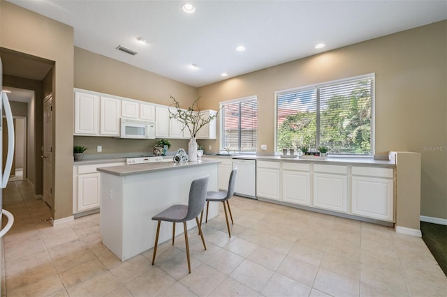 kitchen featuring white cabinetry, a kitchen island with sink, light tile patterned floors, and white appliances