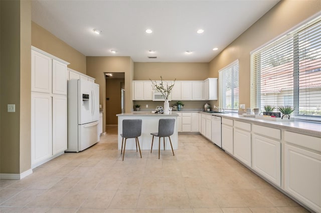 kitchen with white cabinets, a kitchen bar, white appliances, and a kitchen island