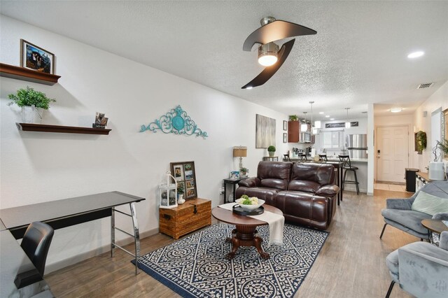 living room featuring hardwood / wood-style flooring, ceiling fan, and a textured ceiling