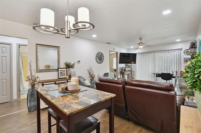 dining area featuring a textured ceiling, ceiling fan with notable chandelier, and light wood-type flooring