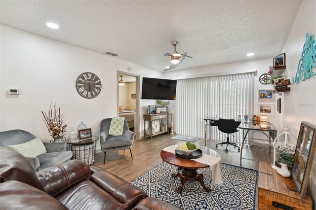 living room featuring dark hardwood / wood-style floors, ceiling fan, and a textured ceiling