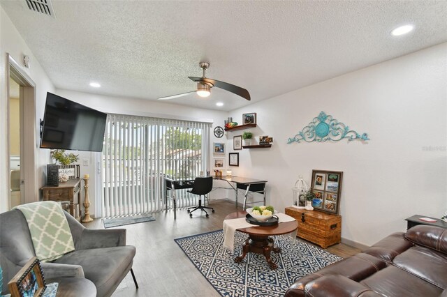 living room with ceiling fan, a textured ceiling, and light wood-type flooring